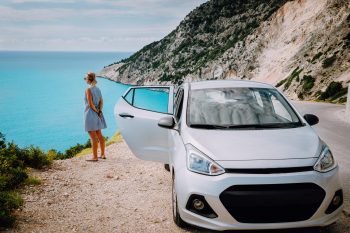 Women near rented car with open door enjoying Myrtos Beach. Travel vocation concept. Kefalonia Women near rented car with open door enjoying Myrtos Beach. Travel vocation concept. Kefalonia